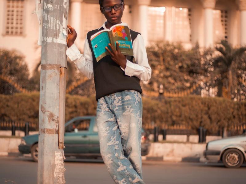 A student in glasses reading a nursing textbook outside a campus building