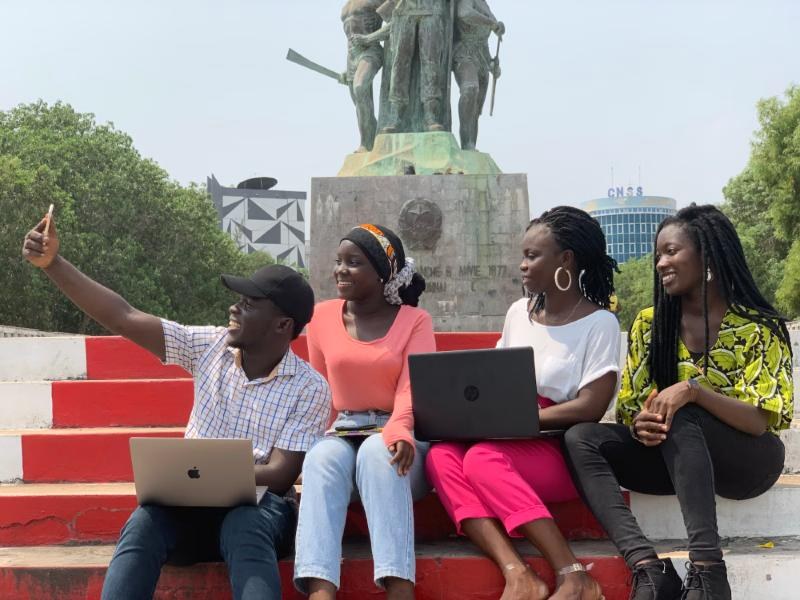 Five students with laptops taking a selfie on red campus steps