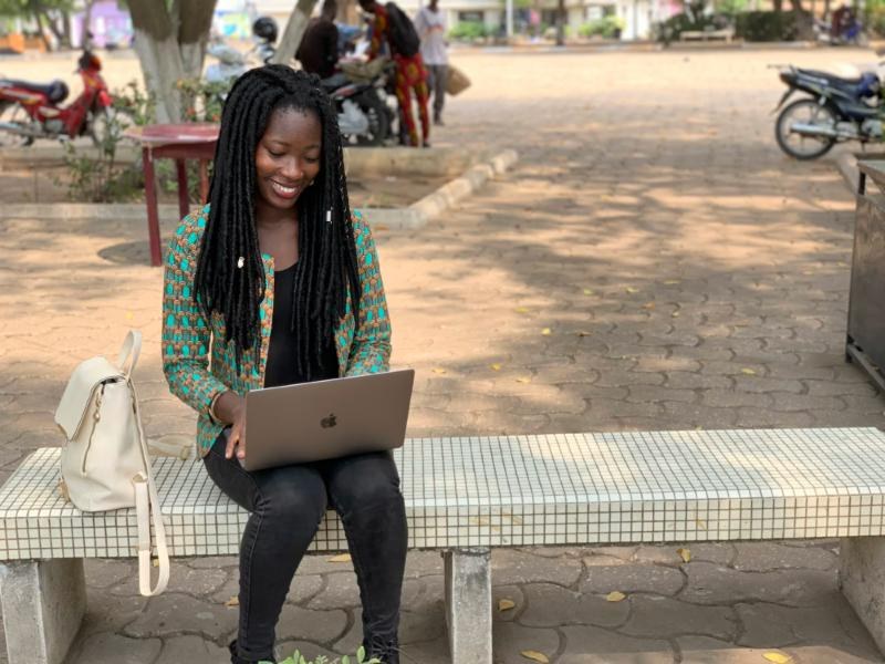 A student with a laptop smiling on a campus bench